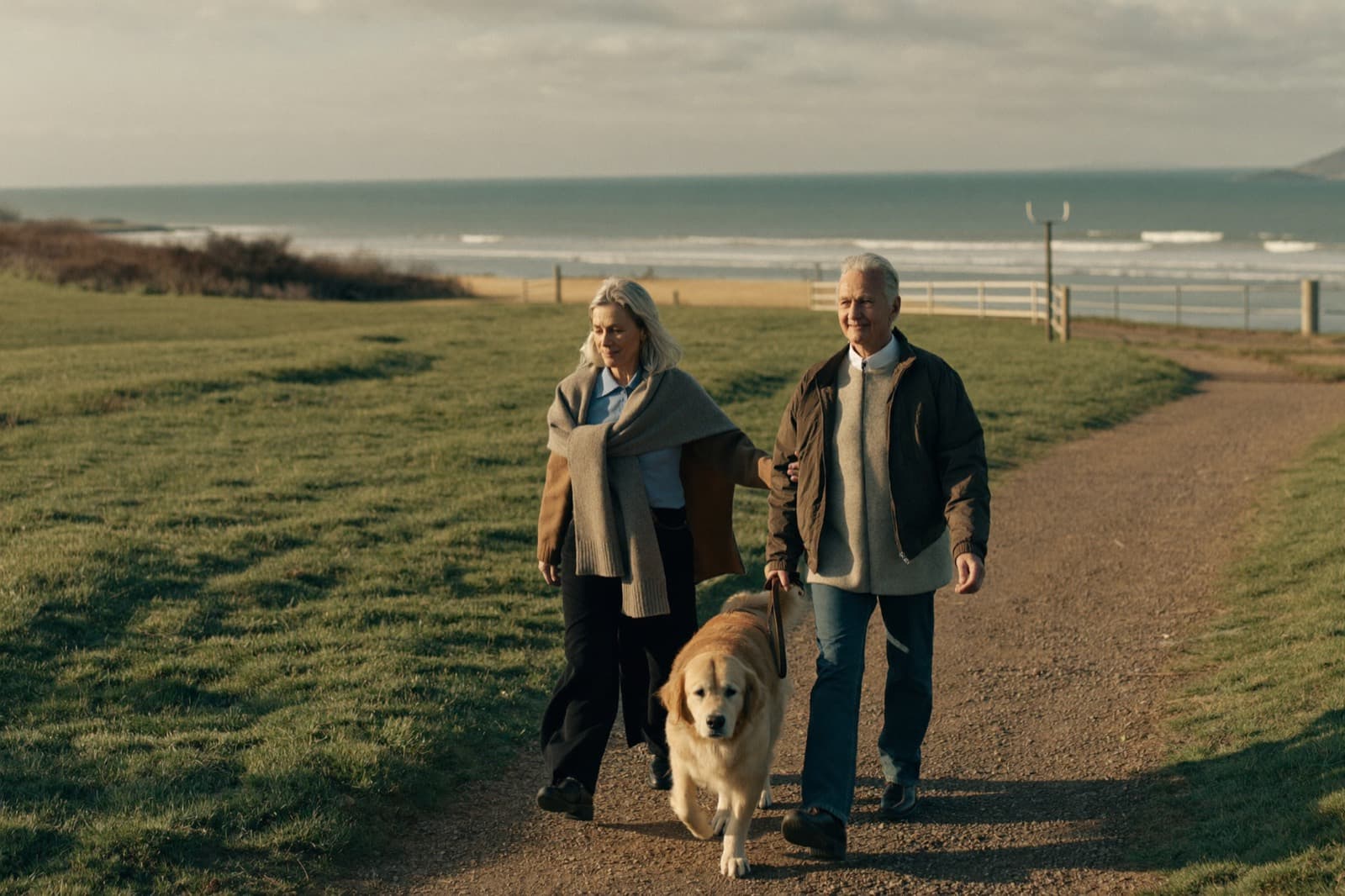 A retired couple walking their golden retriever along a coastal path