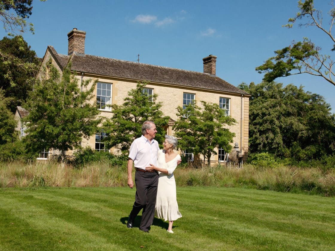 A couple walking across the lawn in front of their country house