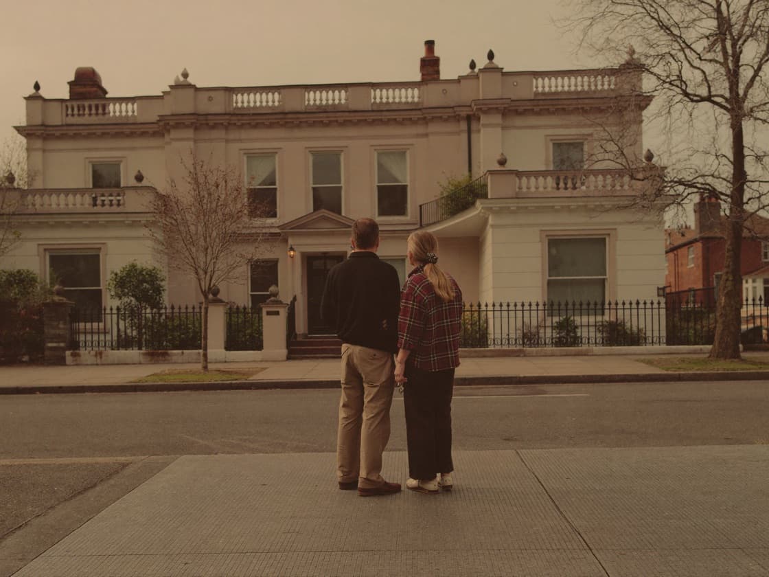 A couple standing on the pavement looking up at a large period house