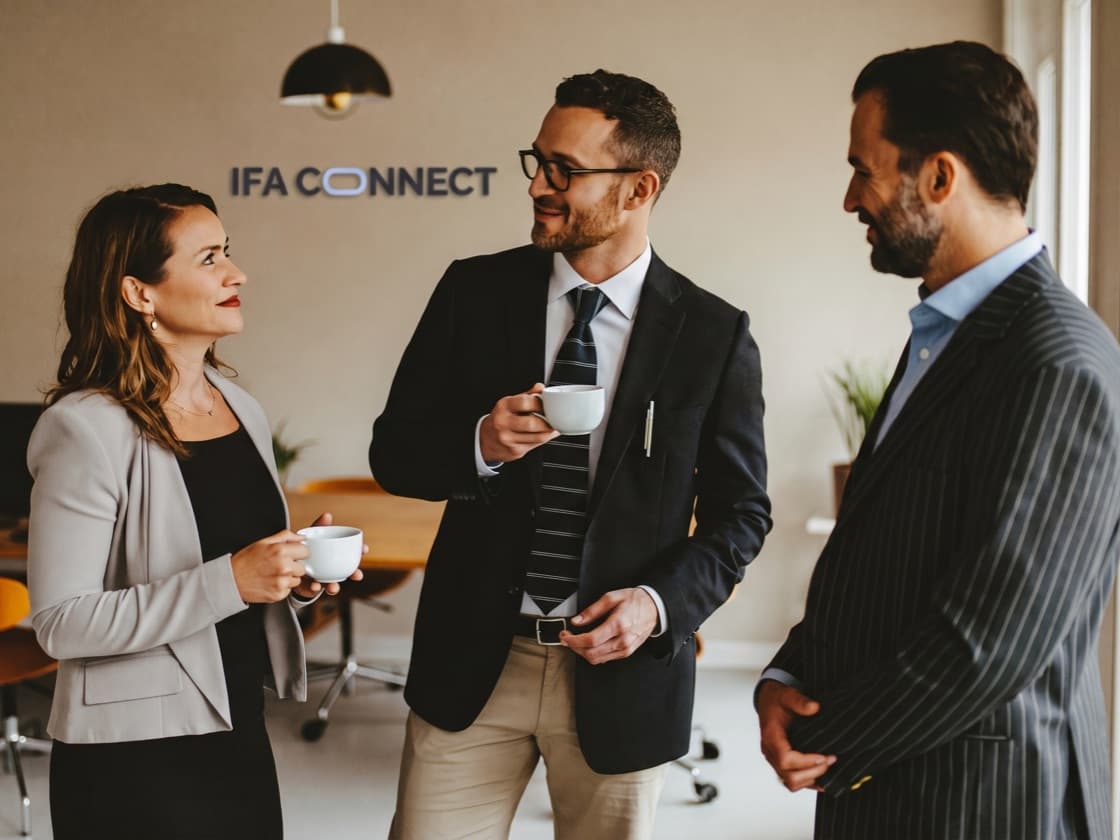 Three members of the IFA Connect team talking over coffee in the office